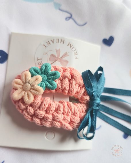 A soft peach shade hair accessory adorned with flowers and a teal ribbon.