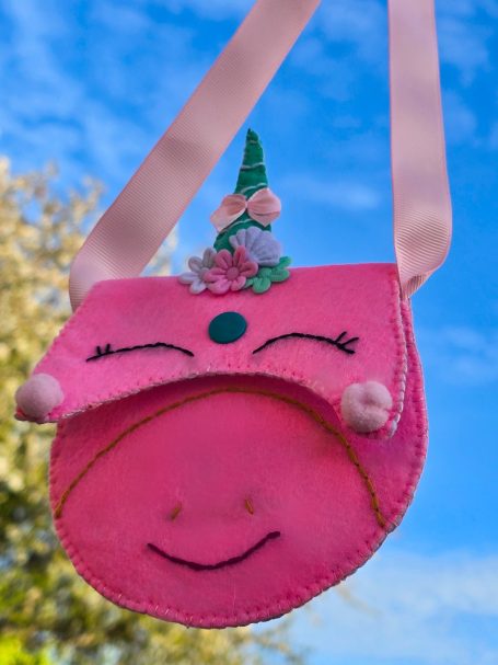 A pink unicorn-themed bag with a smiling face and decorative features.
