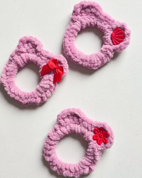 Three pink hair ties shaped like cat heads, each with a red bow or flower accent.