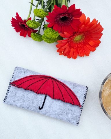 Under the Red Umbrella - Felt Pouch Grey pouch with a red umbrella design on the front.