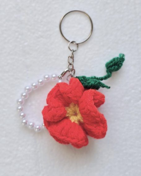 Orange flower with a green leaf keychain attached to a pearl bracelet-style detail.