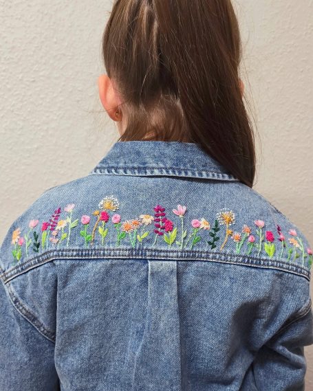 Back of a denim jacket featuring colourful floral embroidery.