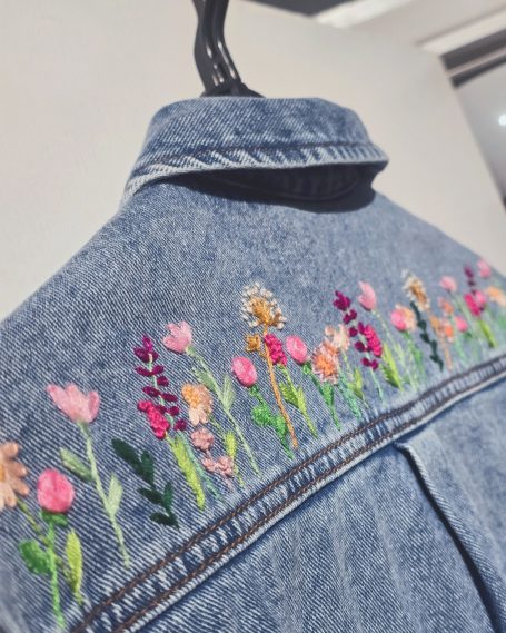 Back of a denim jacket featuring colourful floral embroidery.