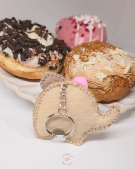 A cute elephant keychain with a pink bow, beside two donuts on a plate.