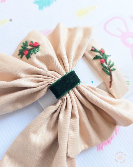 Champagne Christmas bow embroidered with festive mistletoe details and matching hair clip.