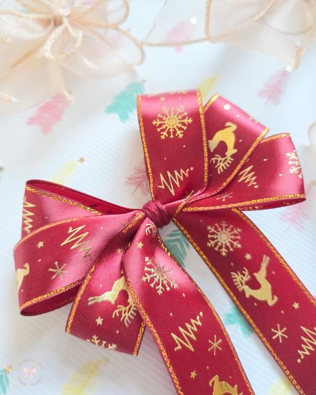 Set of four Christmas decorations: red ribbon bow with gold festive patterns of reindeer and Christmas trees and three small, gold bows.