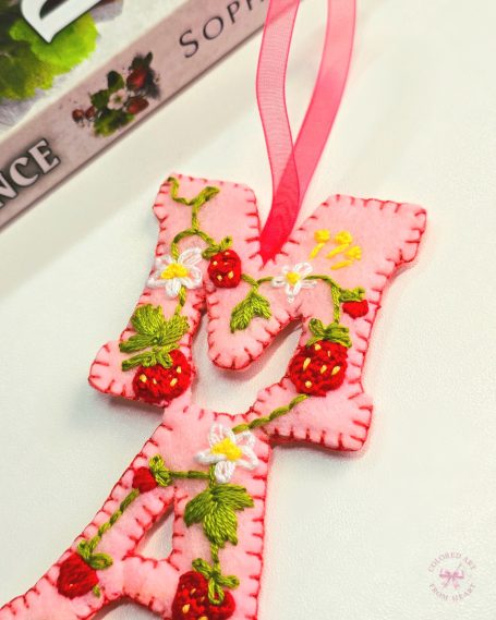 A pink strawberry-themed bookmark with decorative stitching and a ribbon.