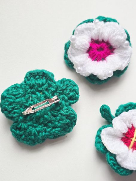 Three crocheted flowers with white petals and green leaves, featuring pink and yellow centres.
