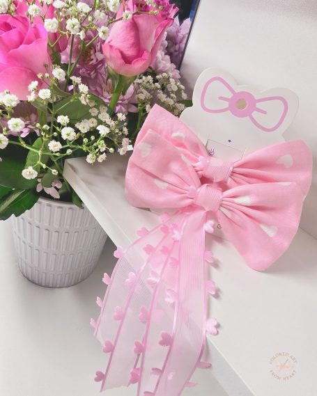 Set of two pink bows with ribbons with hearts, beside a bouquet of pink flowers.