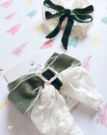 Two hair accessories: a green velvet bow and an ivory lace ribbon with a gem.
