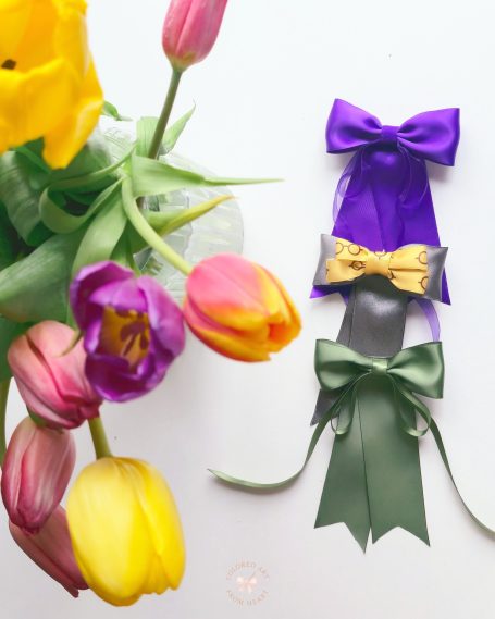 Handmade decorative bows set of three, in purple, gold and green next to vibrant tulips.