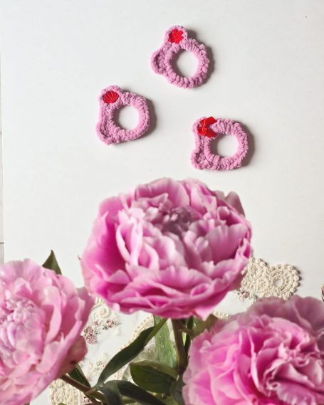 Three pink hair ties shaped like cat heads, each with a red bow or flower accent.