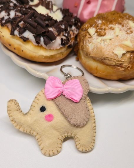 A cute elephant keychain with a pink bow, beside two donuts on a plate.
