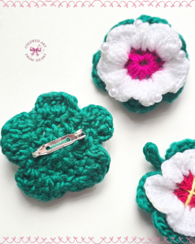 Blush Bloom - Crocheted Brooches/Pins Three crocheted flowers with white petals and green leaves, featuring pink and yellow centres.