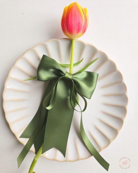 Handmade olive-green fabric hair bow displayed with a colourful tulip.