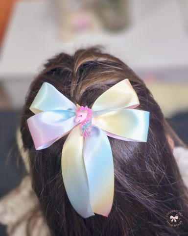 Dreamy Unicorn - Mini Bow Large pastel rainbow bow with a unicorn detail, styled in hair.