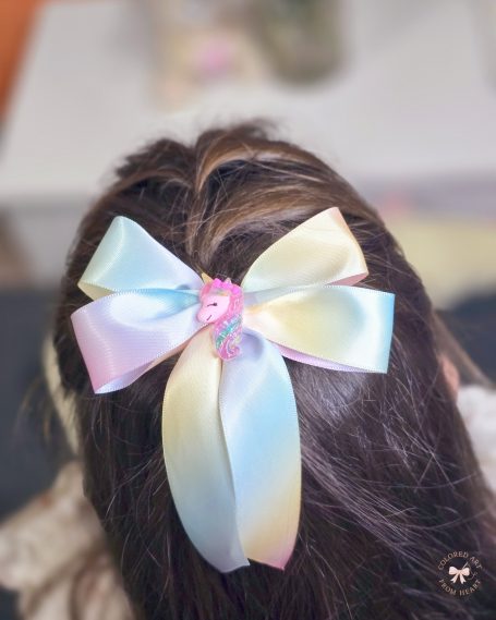 Large pastel rainbow bow with a unicorn detail, styled in hair.