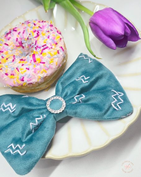 Handmade velvet bow in a luminous turquoise shade, with Aquarius symbol embroidered several times in lilac.