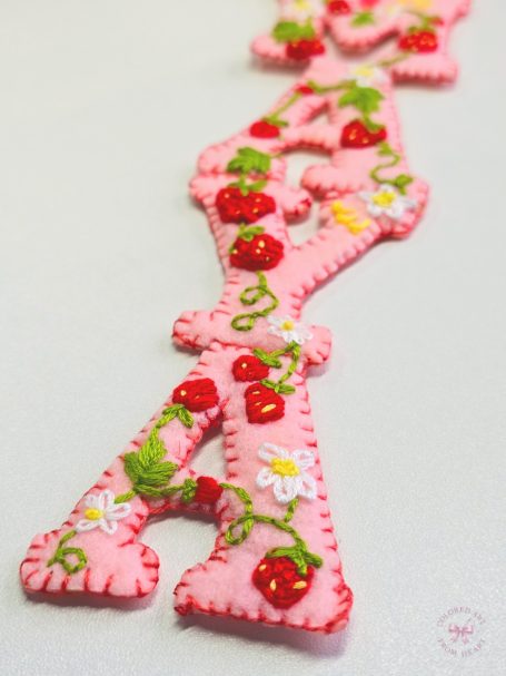 A pink strawberry-themed bookmark with decorative stitching and a ribbon.