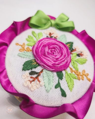 Positive Rose – Decoration Embroidered floral design featuring a pink rose and green leaves, adorned with a ribbon.
