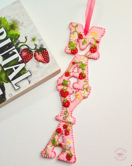 A pink strawberry-themed bookmark with decorative stitching and a ribbon.