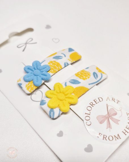 Set of two handmade flower-shaped hair clips in yellow, blue and white.