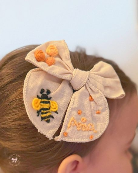 Handmade personalised linen hair bow embroidered with a bee, honeycomb details and the name "Aria".