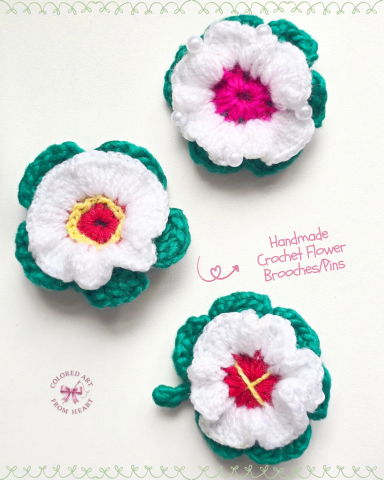Blush Bloom - Crocheted Brooches/Pins Three crocheted flowers with white petals and green leaves, featuring pink and yellow centres.