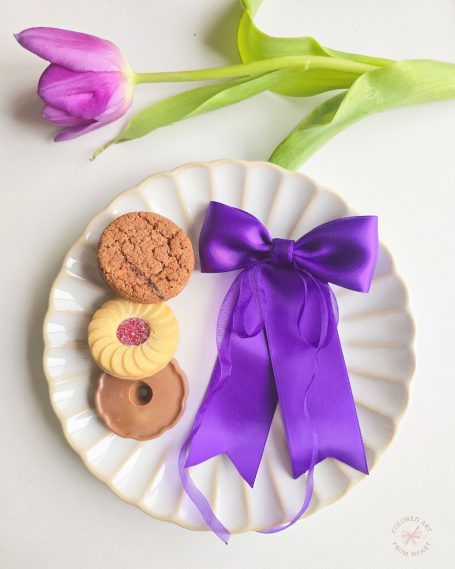 Handmade deep purple fabric hair bow displayed with cookies and a pink tulip.
