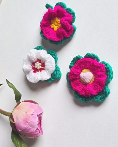 Blush Bloom - Crocheted Brooches/Pins Three crocheted flowers with white petals and green leaves, featuring pink and yellow centres.