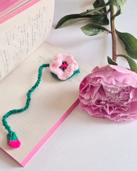 A pink flower bookmark beside a pink peony on an open book.