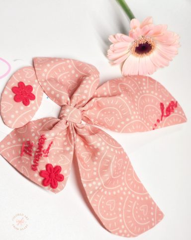 The answer is... Love - Bow and Hair Clip Coral pink fabric bow with red embroidered text "The answer is love", paired with a matching hair clip.
