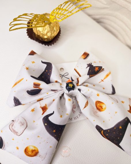 White bow with Harry Potter-themed patterns, accompanied by a gold foil chocolate with golden snitch wings.