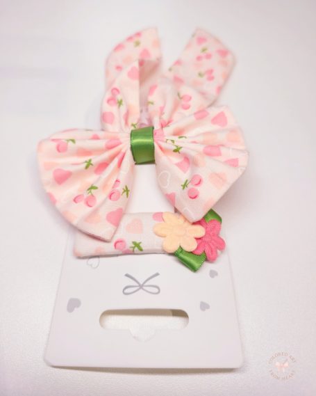 Set featuring a statement butterfly- bow and a matching clip. Soft pink fabric with hearts and cherry prints and a fresh touch of green.