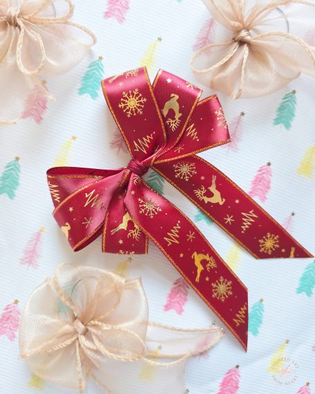 Set of four Christmas decorations: red ribbon bow with gold festive patterns of reindeer and Christmas trees and three small, gold bows.