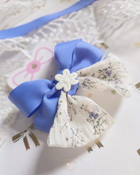 a handmade bow in soft blue tones, delicate floral fabric and a tiny white flower in the center.