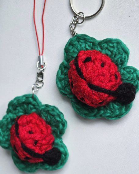 Two handcrafted keychains/ phone accessories featuring red ladybugs on green leaves.