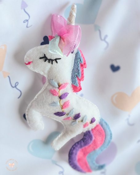 A white unicorn toy with a pink bow and colourful mane on a patterned background.