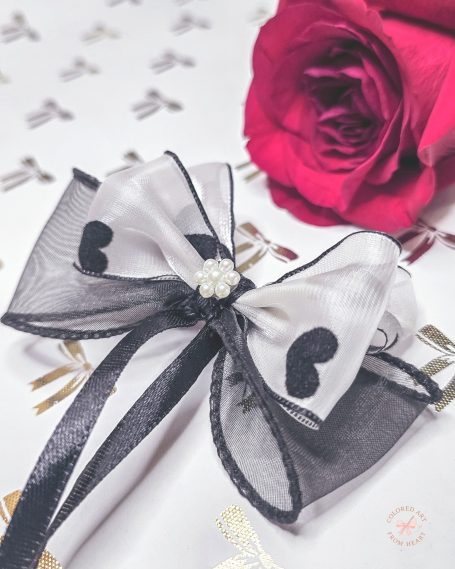 A black and white bow with heart patterns, adorned with a pearl, beside a red rose.